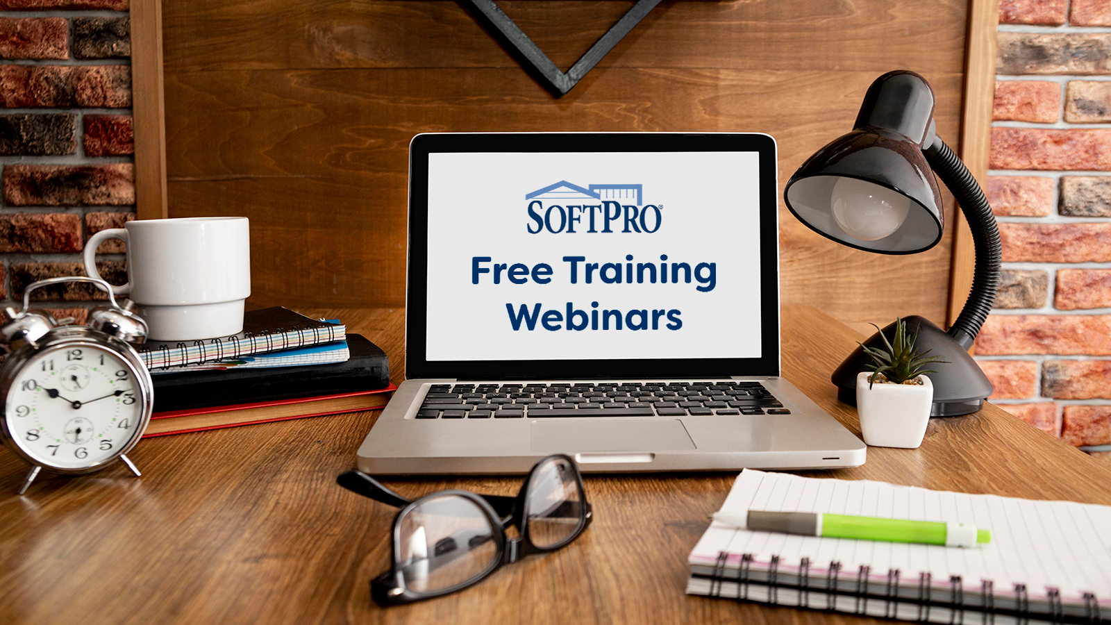 Laptop sitting on desk with glasses and notebook. Screen displays the text "SoftPro Free Training Webinars" in navy blue on a white background.