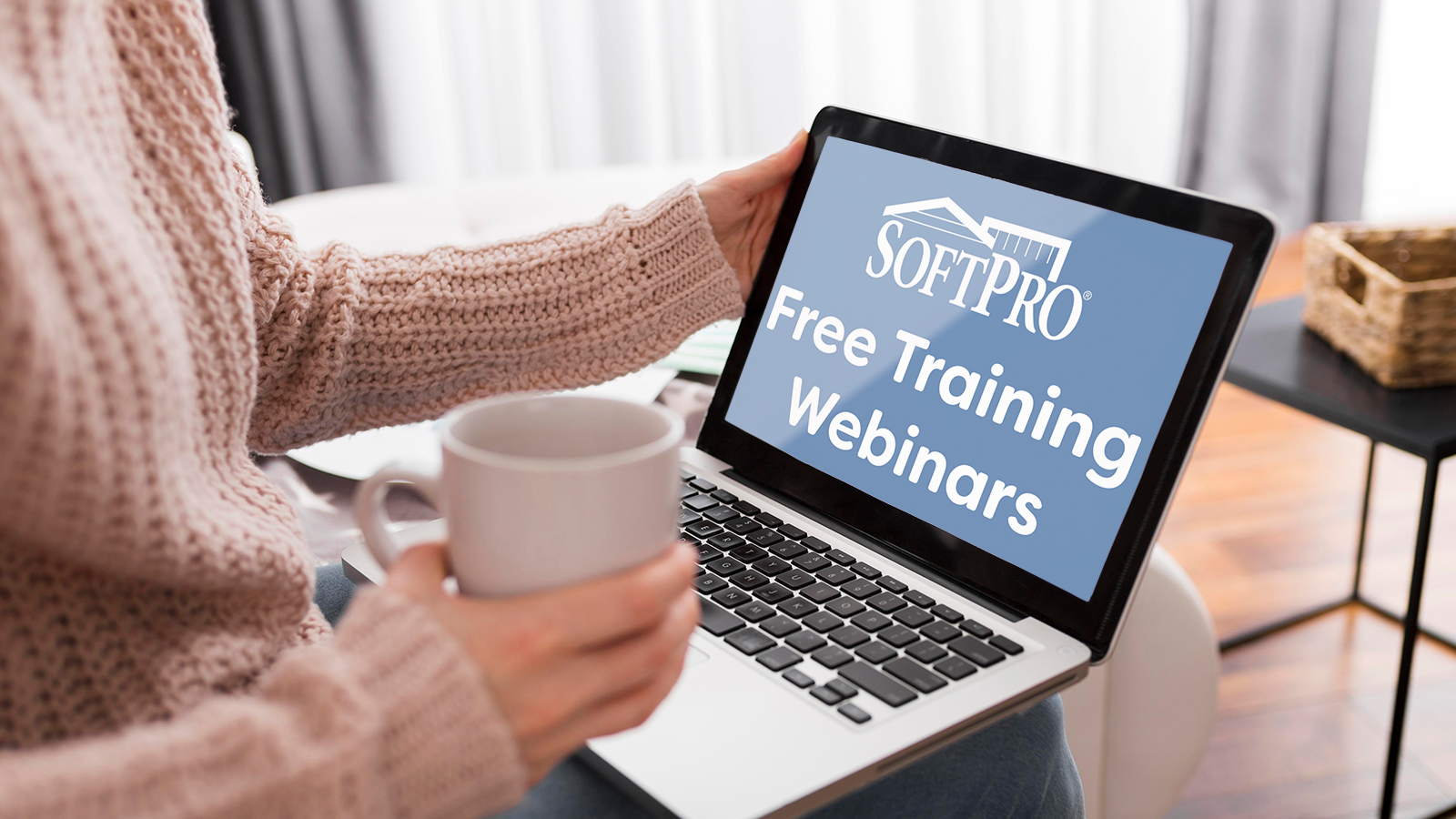 A laptop open on a person's lap. Laptop screen displays the text "SoftPro Free Training Webinars" in white on a light blue background