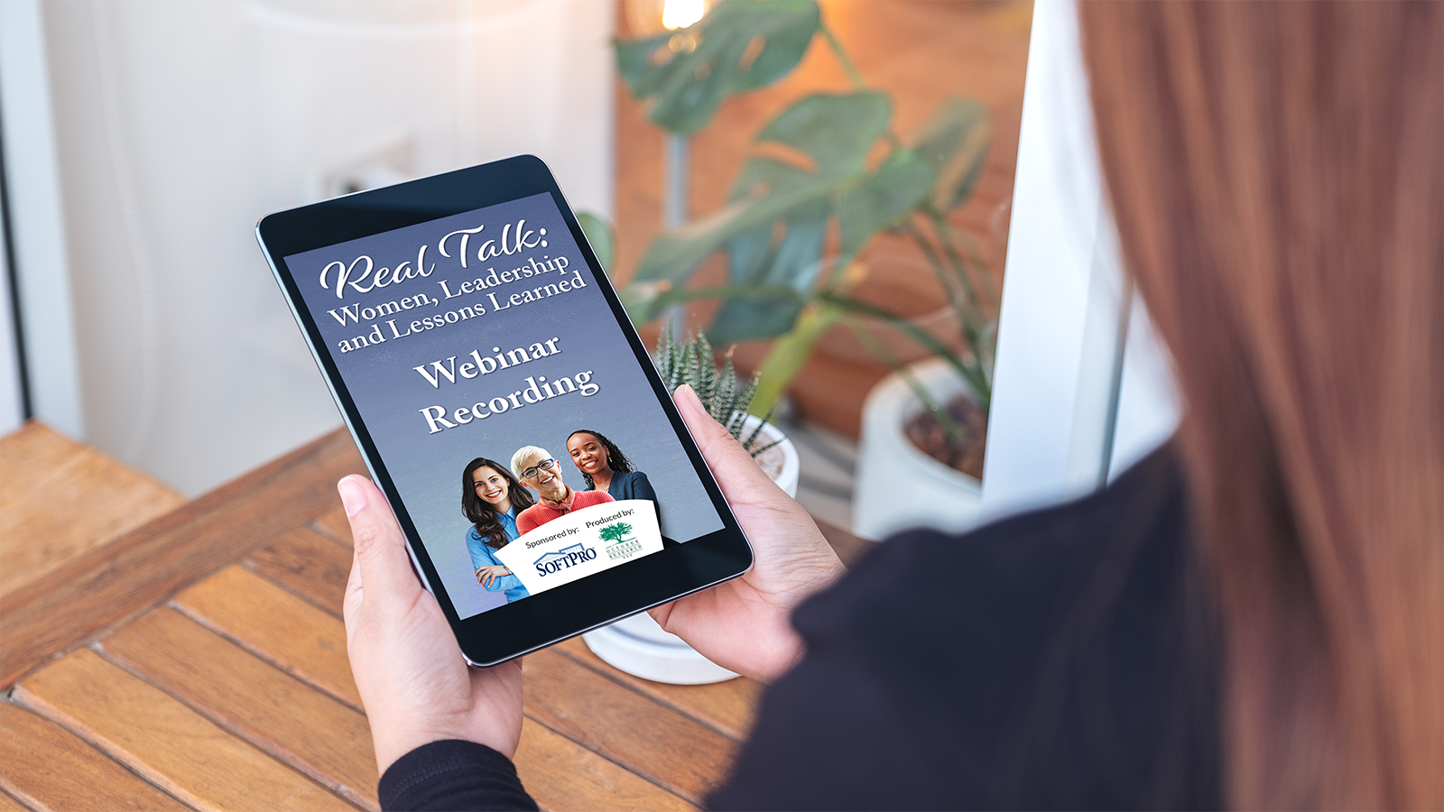 Person holding a tablet displaying a webinar recording titled “Real Talk: Women, Leadership and Lessons Learned,” sponsored by SoftPro.