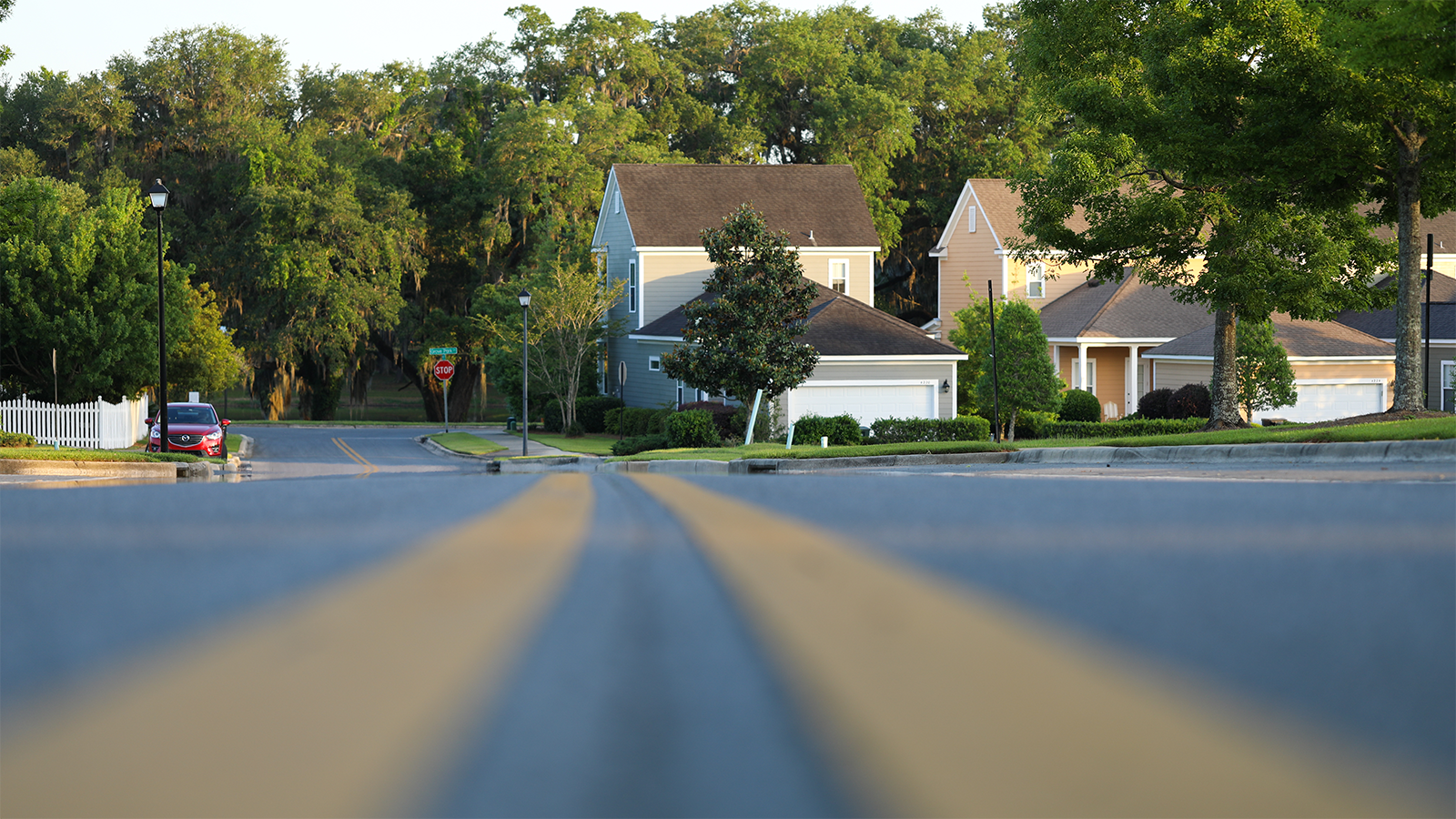 Low angle photograph of an asphalt road with double yellow lines leading to a line of suburban homes